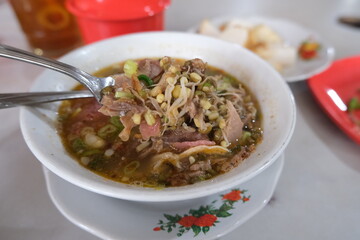 Bowl of sroto, a traditional Indonesian beef soup with bean sprouts, herbs, and savory broth, served hot with rice cakes on the side.
