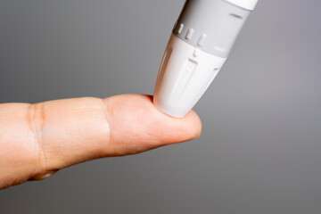 A close-up of a lancet device poised to prick a person's fingertip for a blood sample.

