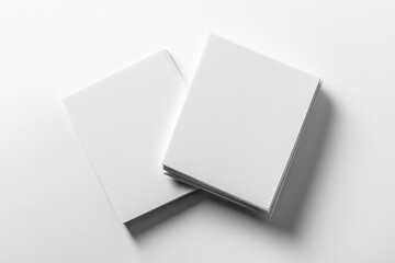 Two stacks of blank white paper sheets placed on a smooth white surface creating soft shadows, minimalistic and clean composition