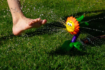 Watering flower sprinkler brings joy as child playfully runs barefoot in the grass on a sunny day