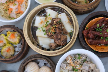 Top-down view of various dim sum dishes including chicken feet, dumplings, siu mai, and steamed rice rolls served in bamboo containers.
