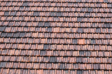 Repetitive layout of traditional clay roof tiles, featuring a mix of red and dark weathered tones in a geometric pattern.
