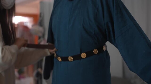 Traditional Chinese costume detail showing a person adjusting the belt on a blue robe