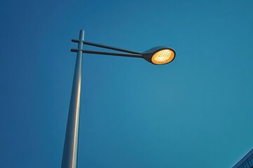 modern street lamp glowing warmly in the early evening against a clear blue sky with a corner of a building visible on the right