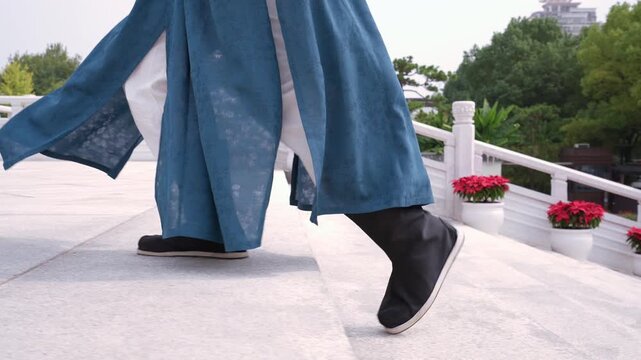 A person in traditional blue hanfu walking gracefully on a stone bridge in a classical garden