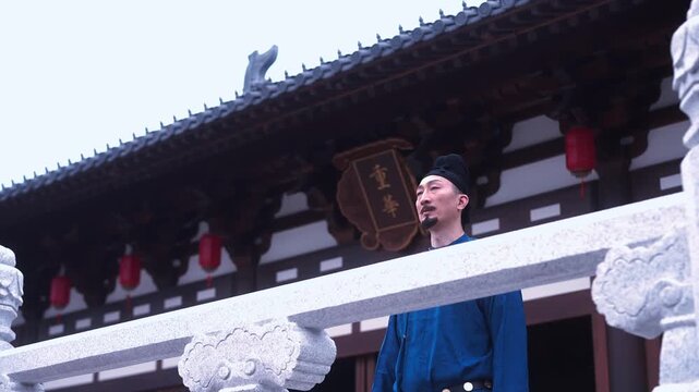 A middle-aged man in blue robe stands on traditional Chinese architectural veranda looking upward at the eaves