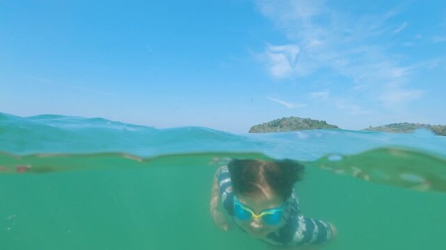 Young boy snorkeling and swimming independently in turquoise sea, over-under perspective.