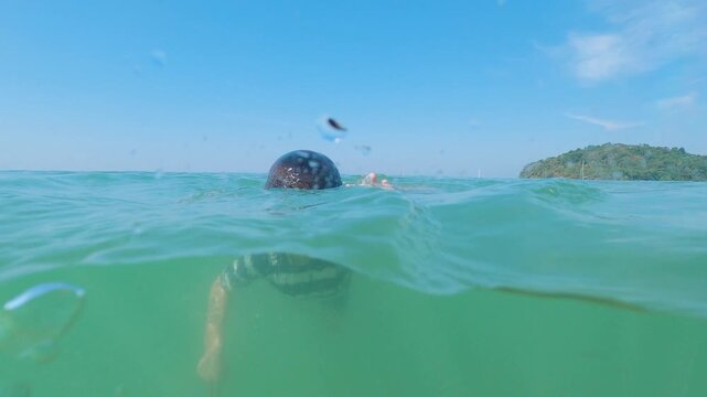 Young boy snorkeling and swimming independently in turquoise sea, over-under perspective.