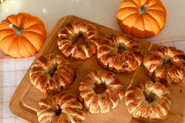Freshly baked pumpkin-shaped pastries with decorative mini pumpkins on wooden board