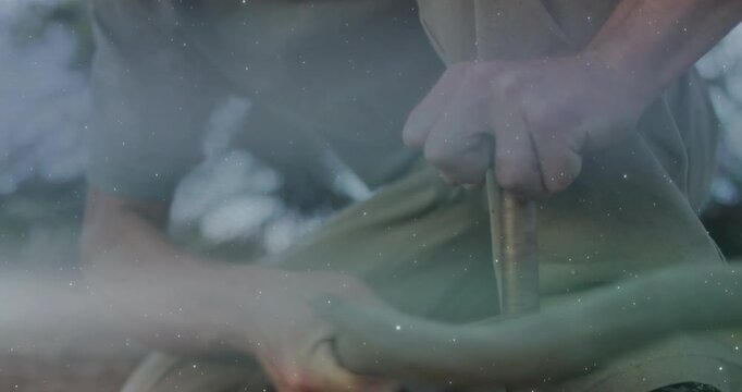Man kneeling inserting spindle into fireboard, spinning and sparking with heat gauge for survival