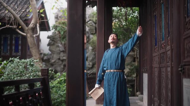 A man in traditional Chinese attire leans against a wooden doorway while gazing upward in a classical garden courtyard with lush greenery