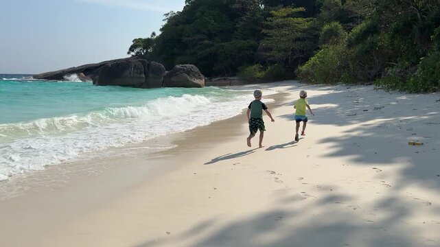 Children playing on white sandy beach by turquoise sea waves at Similan Islands, Thailand, tropical vacation scene.