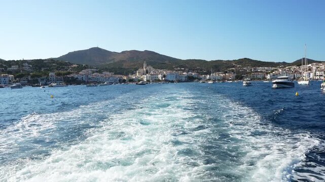 White boat trailing along coastline, revealing scenic mediterranean seascape near cadaques with white houses, blue sky, and calm waters characteristic of costa brava's picturesque landscape
