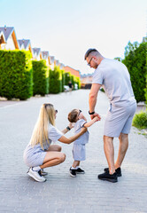 Family enjoying playful moment on street. Parents playfully engage with their young child on a sunny street, surrounded by houses and greenery in the background.