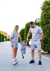 Obraz premium Family walking outdoors together. Couple and their young child happily walk along a tree-lined street, sharing joyful moments on a sunny day.