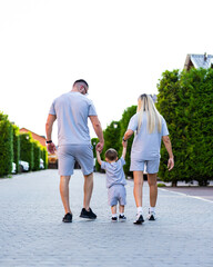 Obraz premium Family stroll on a sunny day in shorts. A family walks hand in hand along a tree-lined path, enjoying a sunny day while wearing matching outfits.