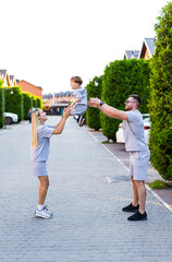 Parents playfully lift child outdoors. A happy family plays outside, with parents joyfully lifting their young child in a neighborhood.
