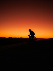 Sunset Mountain Bike Adventure: Solo Rider's Silhouette on Desert Trail Against a Fiery Orange Sky