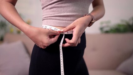 Determined woman measures waist body for fitness health goals tracking personal progress achieving healthy lifestyle daily discipline at home indoor setting