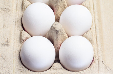 Close-up of white eggs in cardboard tray on white background.