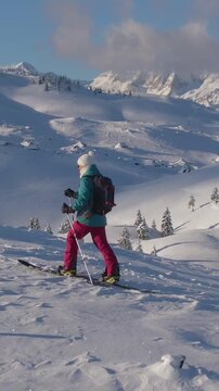 DRONE: Spectacular shot of a snowy valley as young woman hikes along a meadow during a ski touring trip in Velika Planina. Fit female splitboarder hikes up a scenic mountain in picturesque Slovenia.