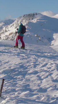 AERIAL, COPY SPACE: Young female splitboarder observes the picturesque winter scenery after reaching the mountaintop. Picturesque snowy landscape surrounds woman ski touring in Slovenian mountains.