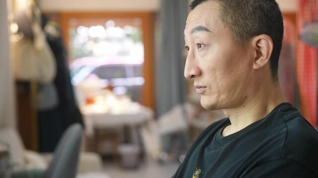 Middle-aged Asian man in profile gazing thoughtfully indoors with soft natural lighting