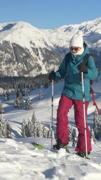 CLOSE UP: Fit Caucasian woman ski touring in Velika Planina on a perfect sunny winter day. Young female tourist on splitboarding trip hikes up a snowy hill. Splitboarder ascends up a scenic mountain.