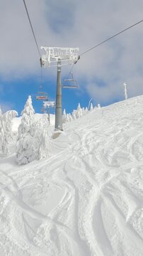POV: Riding the ski lift over the tracked slopes of a ski resort in the picturesque Slovenian mountains. First person view of a chairlift ride over the vast ski resort slopes covered in crud snow.