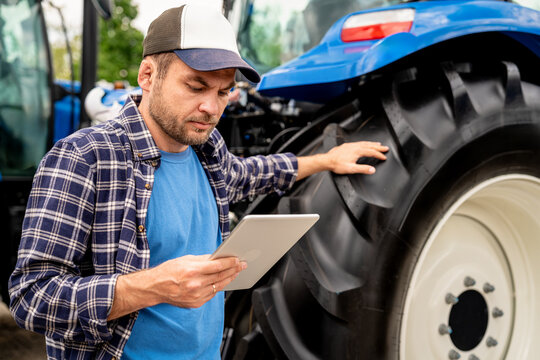 Man farm worker using digital tablet standing neat tractor outdoors