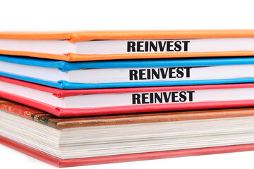 Business and reinvest concept. Copy space. REINVEST word on the ends of notebooks lying on top of each other on a white background
