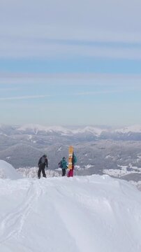 AERIAL: Flying around three ski tourers after reaching the snowy mountaintop overlooking the spectacular Slovenian countryside. Tourists observe the winter landscape before splitboarding down mountain