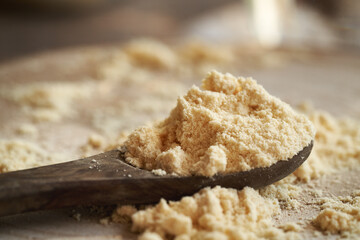 A heap of whey protein powder on a wooden spoon, closeup