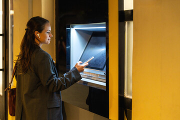 Woman using smartphone for contactless ATM cash withdrawal on city street at night © Barillo Images