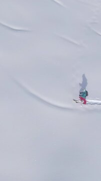 DRONE: Scenic drone shot of wintry landscape surrounding a female ski tourer powder chasing in the Julian Alps. Fit woman on active vacation hikes up a snowy meadow during a fun splitboarding trip.