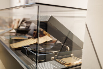 An antique gramophone in a wooden case stands in a glass display case.