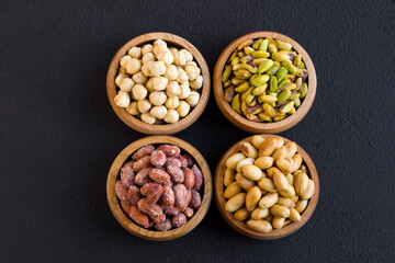 Pistachios, hazelnuts and peanuts were designed in bamboo bowls on black surface