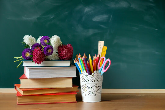 school stationery, flowers and books on table, chalkboard background. symbol of beginning of the school year, teacher's day. Knowledge Day, education concept. back to school. 1 September. copy space