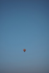 Lonely hot air balloon floats in a vast clear blue sky at peaceful dusk.