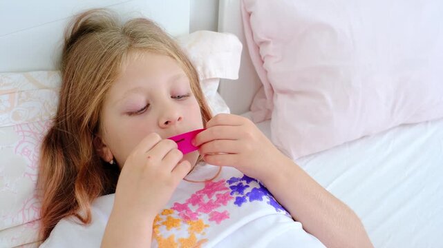 A little girl suffering from adenoids and mouth breathing, lying in bed, puts a sleeping patch on her mouth to sleep with her mouth closed. Nasal breathing habit. anti-snoring patch