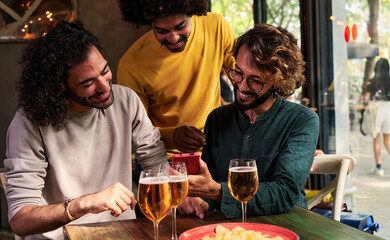 Multiethnic group of male friends together in a bar drinking beer and watching social media on one phone.