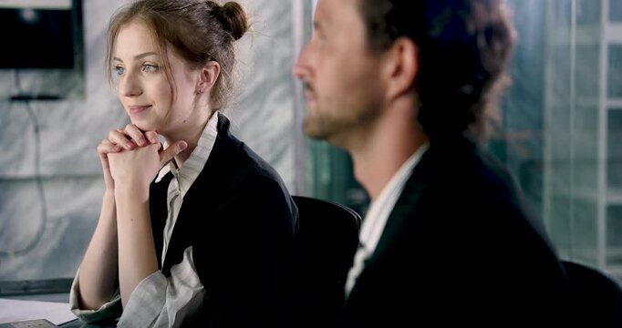 Female professional engaging in corporate conversation with confident smile, seated beside male colleague during meeting, showcasing teamwork and interpersonal communication in office