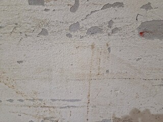 Close-up of a textured, off-white wall with peeling areas exposing gray concrete or plaster beneath..