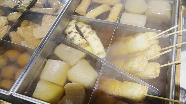 A steaming pot of oden with assorted ingredients like daikon, fish cakes, and skewers simmering in broth-filled compartments.