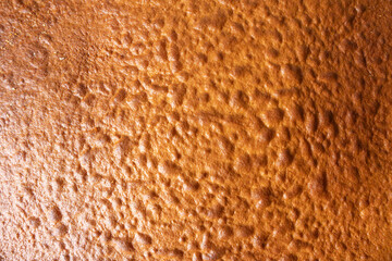 Close-up of a golden-brown, baked cake surface. The texture is airy, uneven, and slightly shiny.