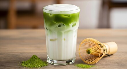 Vibrant and refreshing iced matcha green tea latte in a tall glass, with milk foam, matcha powder, and a traditional bamboo chasen whisk on a wooden table
