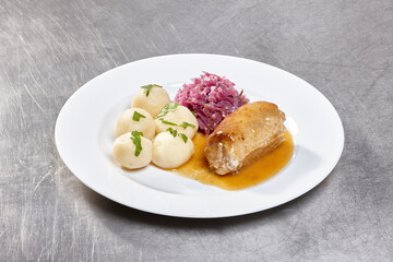 A well-prepared dish featuring tender chicken breast with a rich sauce, potato dumplings, and a serving of pickled red cabbage garnished with fresh herbs