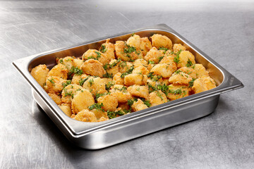Platter filled with golden crispy fried potatoes sprinkled with fresh herbs, displayed at a bustling catering event during daytime, inviting attendees to enjoy a tasty dish