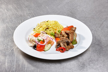 This dish showcases a variety of seasoned meats served alongside yellow rice and a fresh vegetable salad with peppers, onions, and cucumbers, highlighting culinary artistry