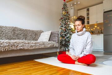 Woman meditating indoors with Christmas decorations during holidays